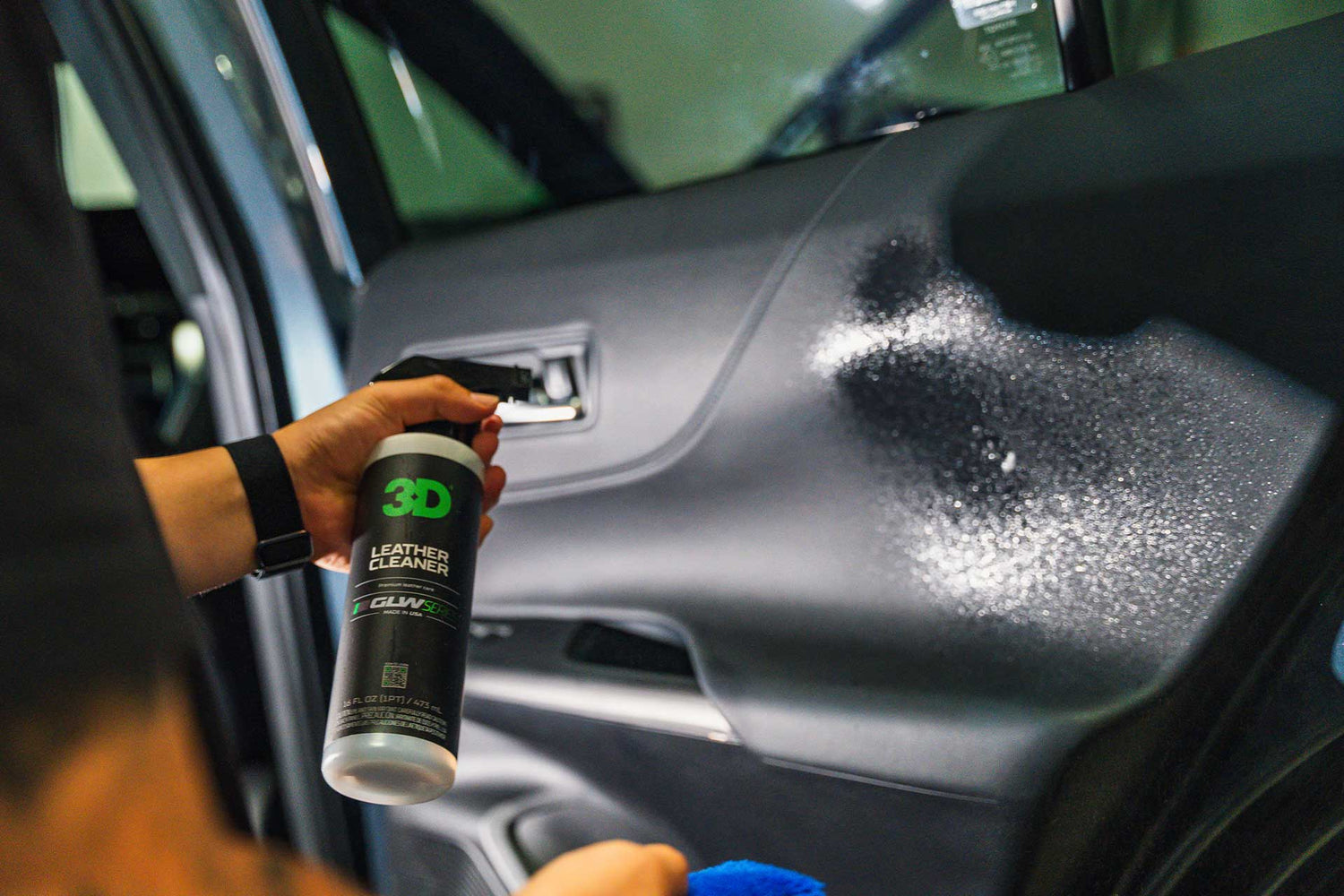 person spraying leather cleaner on leather door panel